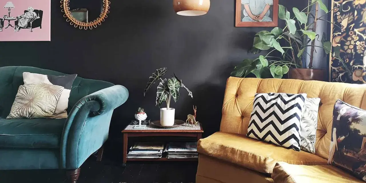 Habitación con poca luz, sofás de terciopelo verde y mostaza, cojines decorativos, plantas y arte en la pared.