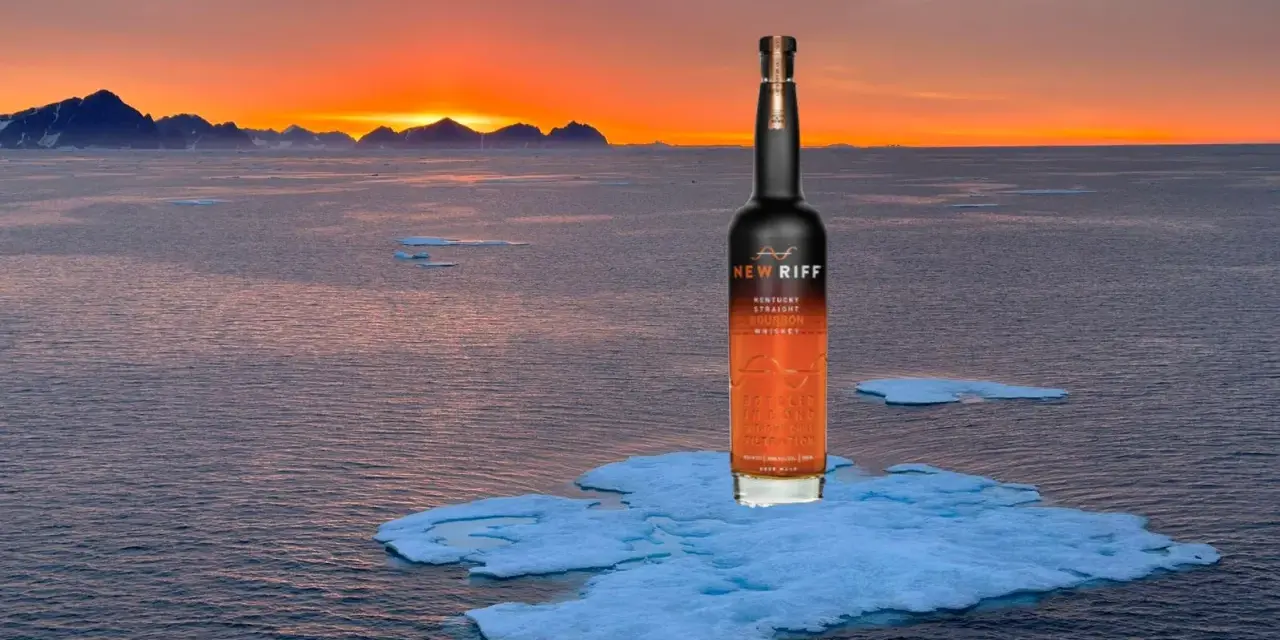 Eine Flasche New Riff Bourbon Whiskey steht auf einer Eisscholle im Meer. Der Sonnenuntergang taucht die Berge am Horizont in warmes Licht. Ein Moment der Ruhe für den besten Whisky der Welt.