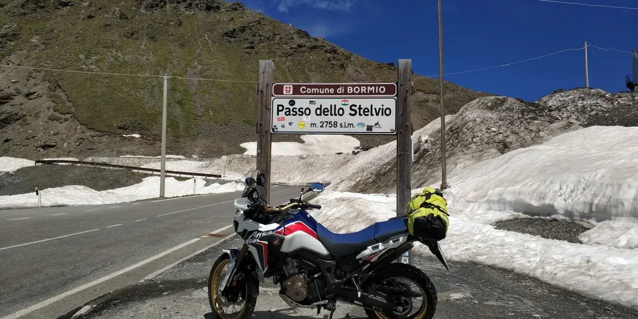 Moto pronta per affrontare il Passo dello Stelvio, con neve ai lati della strada e un edificio in cima alla montagna.