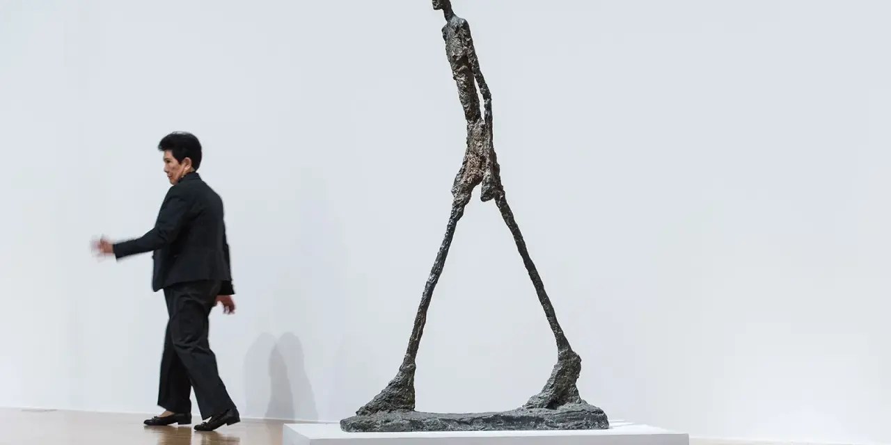 Un homme qui marche, une sculpture élancée, semble se déplacer dans un espace blanc.