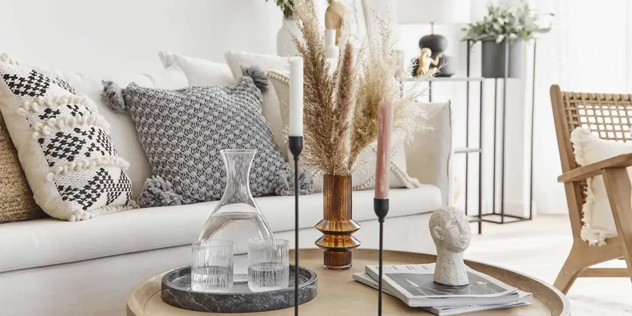 Tavolino rotondo in legno con elementi decorativi che evocano un'atmosfera boho chic: vasi, candele, libri e una scultura di testa.