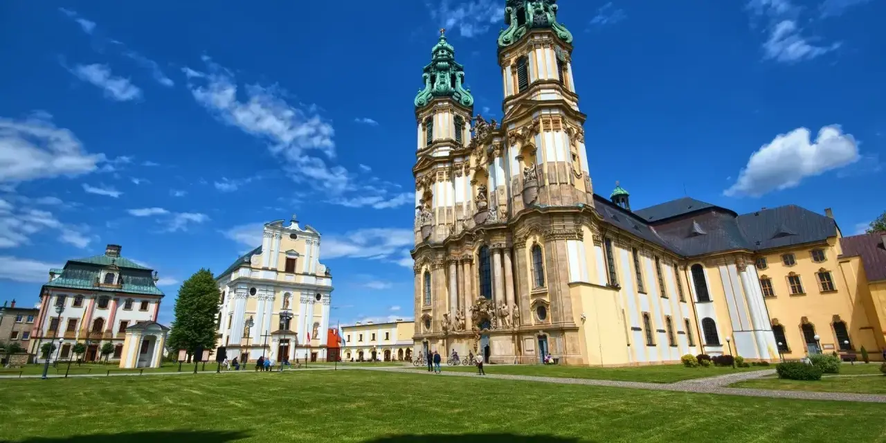 Barokowy kościół i klasztor na tle błękitnego nieba z chmurami. Piękne sanktuaria maryjne w Polsce zachwycają architekturą.