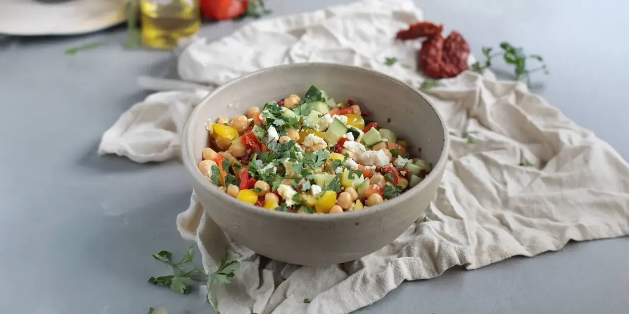 Ein bunter Kichererbsen Salat mit Gurken, Tomaten, Paprika und Feta, garniert mit frischer Petersilie.