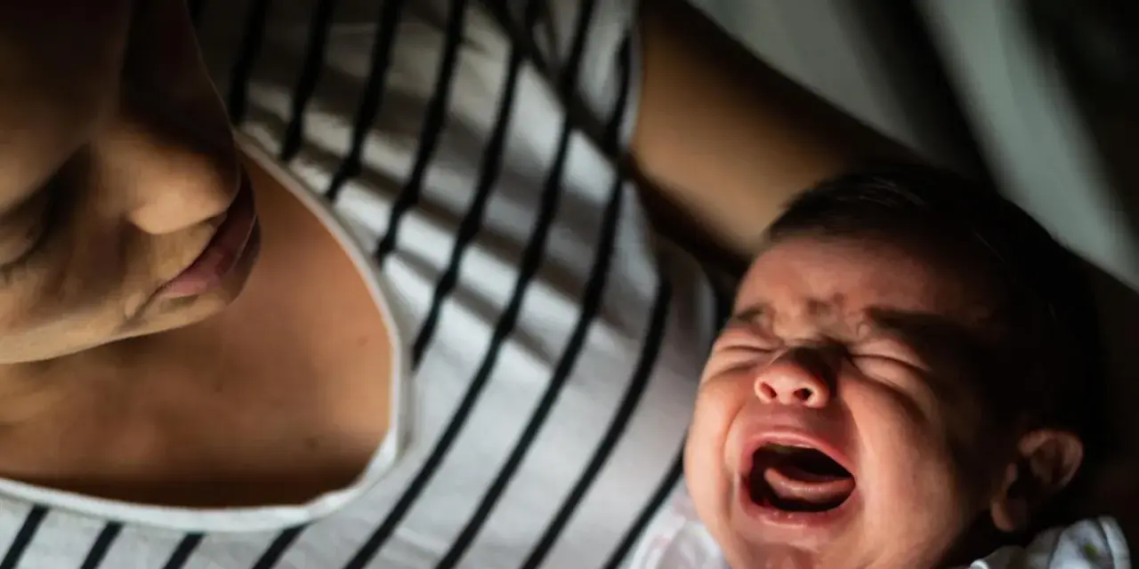 Ein schreiendes Baby, das von seiner Mutter getröstet wird. Vielleicht ein Zeichen für eine frühe Hochbegabung, die sich in intensiven Emotionen äußert.