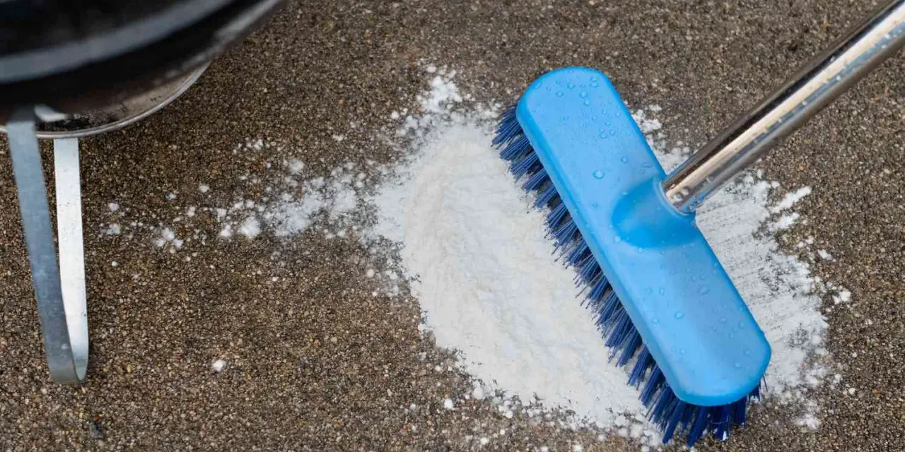 A blue brush is used to scrub a pile of white powder on a concrete patio, demonstrating how to clean concrete patio.