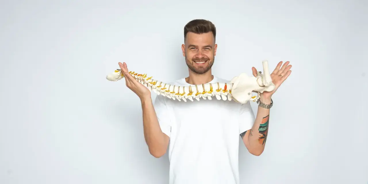 Uśmiechnięty mężczyzna trzyma model kręgosłupa, jakby prezentował jego elastyczność, niczym worek oponowy.