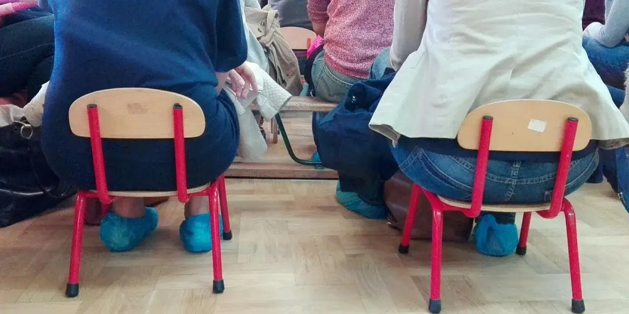 Dostateczny, jaka to ocena? Dzieci siedzą na małych krzesełkach w niebieskich ochraniaczach na buty.
