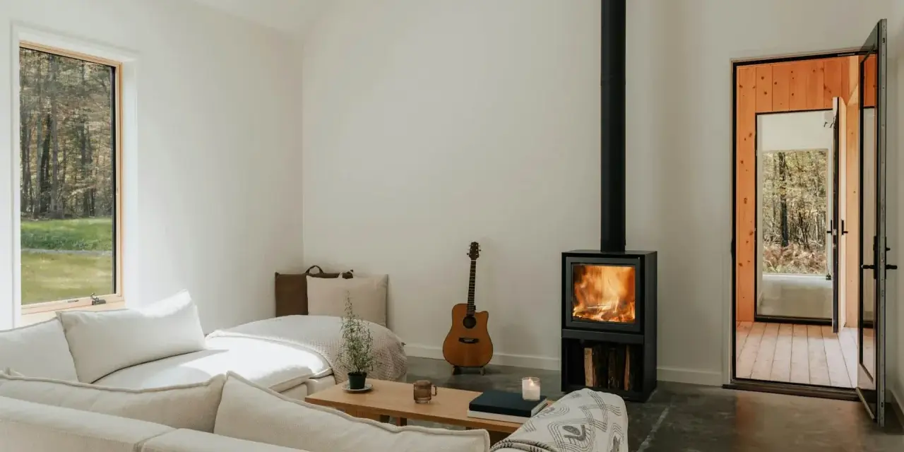 Salon cosy avec poêle à bois allumé, guitare et canapé. Une aide financière pour le tubage de cheminée pourrait rendre ce lieu encore plus chaleureux.