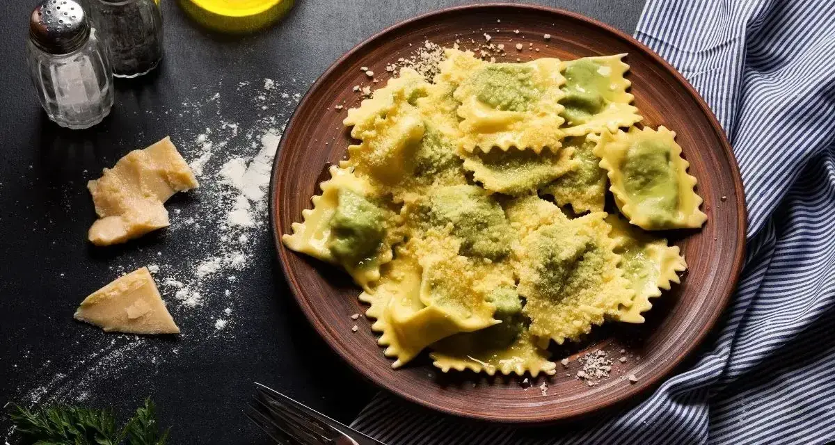 Pyszne ravioli z zielonym farszem, posypane parmezanem. Obok kawałki sera i przyprawy, gotowe do podania.