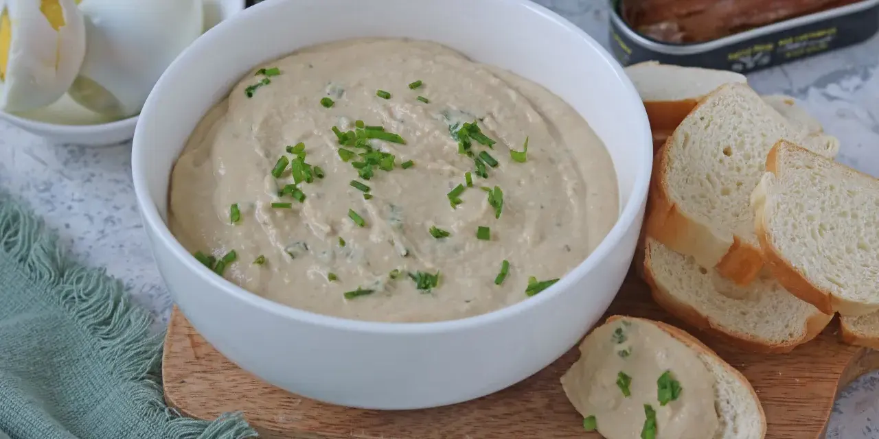Una ciotola di cremosa salsa tonnata con maionese, guarnita con erba cipollina, accanto a pane tostato e uova sode.