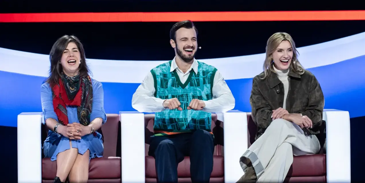 Trzy osoby śmieją się na kanapie, jakby oglądali koło fortuny kiedy w tv.