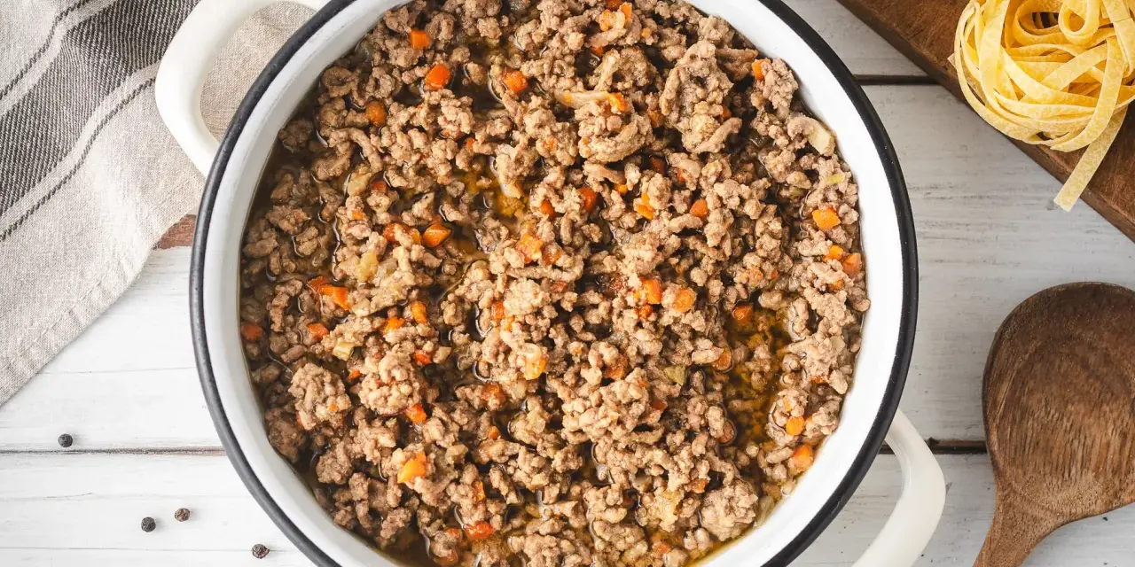 Un saporito ragù bianco in una pentola, pronto per condire la pasta. Pezzetti di carota e cipolla si mescolano alla carne macinata.