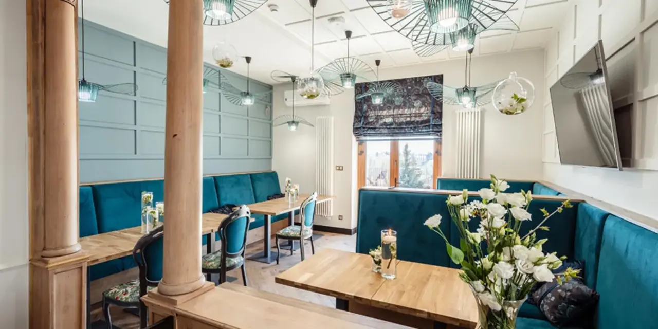 Wnętrze restauracji z turkusowymi kanapami, drewnianymi stołami i ozdobnymi lampami.