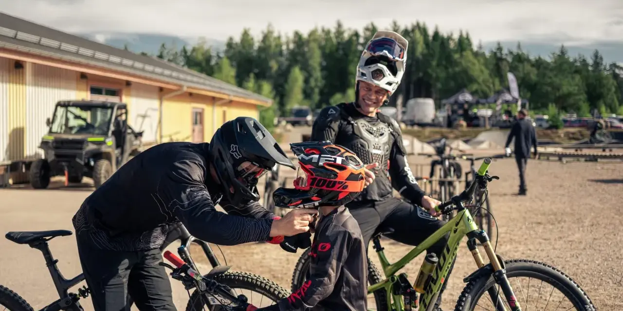 Två cyklister förbereder sig för mtb downhill. En vuxen hjälper ett barn med hjälmen.
