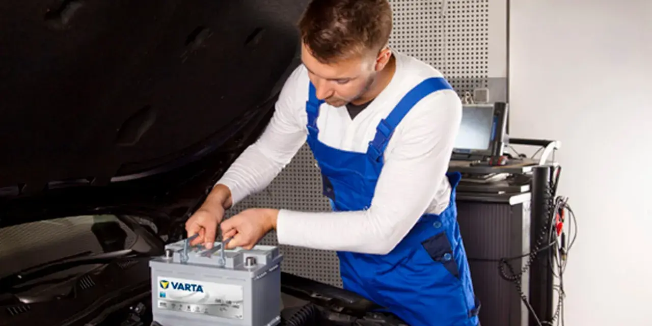 Mechanik w niebieskim kombinezonie wykonuje kodowanie akumulatora Varta w samochodzie.