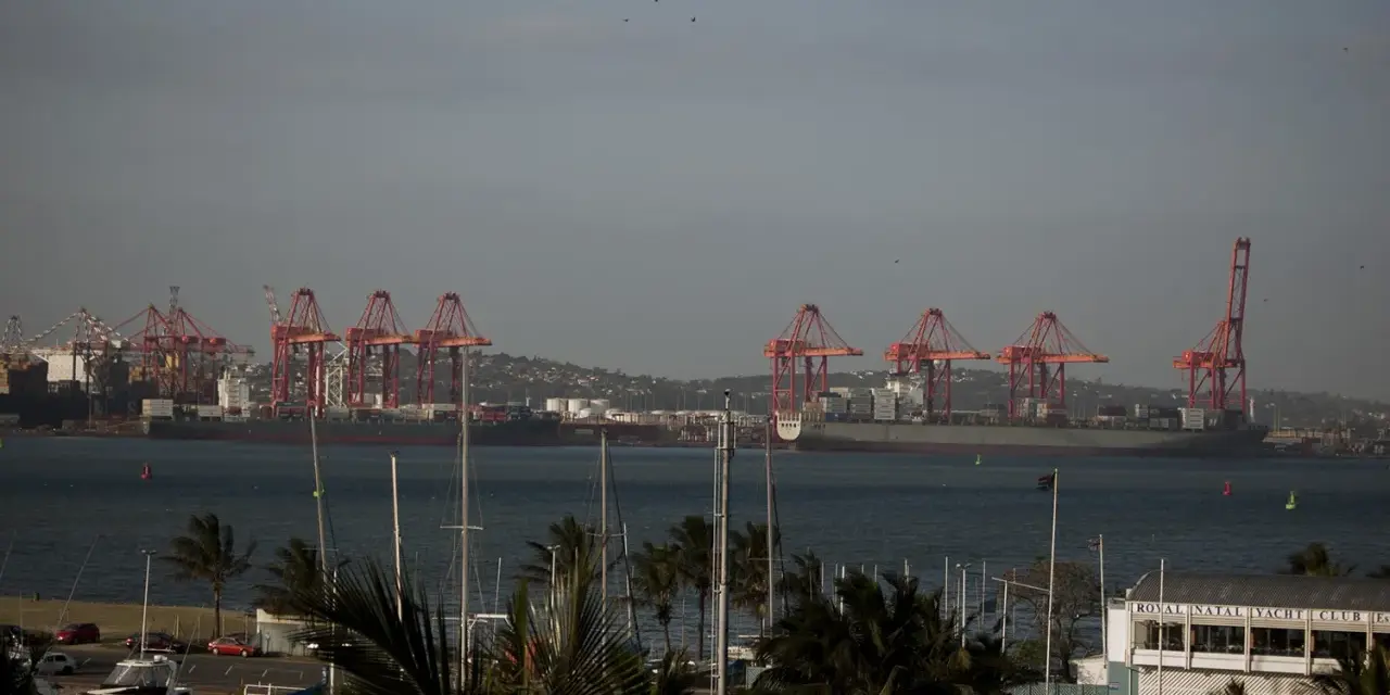 Port w Durban, RPA, z czerwonymi dźwigami portowymi i statkami towarowymi na tle wzgórz. Na pierwszym planie widać maszty jachtów.