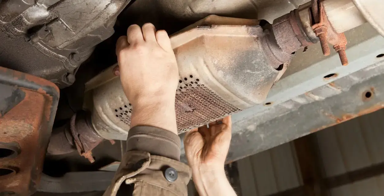 Mechanic inspecting a catalytic converter, a common culprit for why does my car smell like rotten eggs.