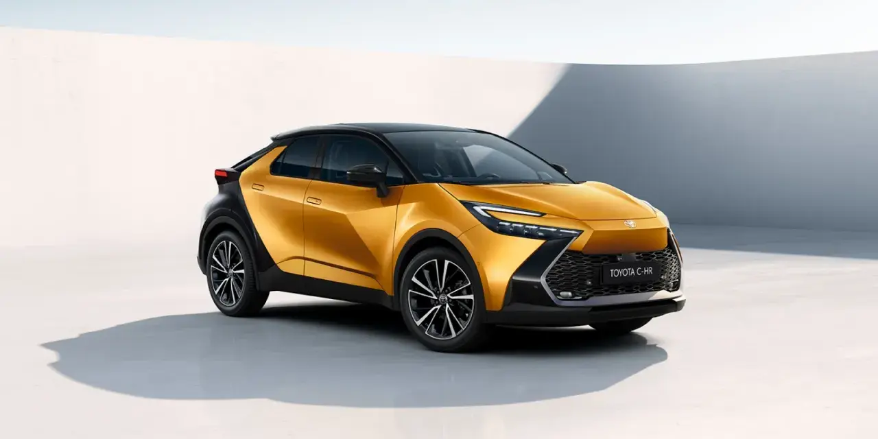 Nowy, złoty Toyota C-HR Hybrid z czarnym dachem prezentuje się dynamicznie na tle minimalistycznej architektury.
