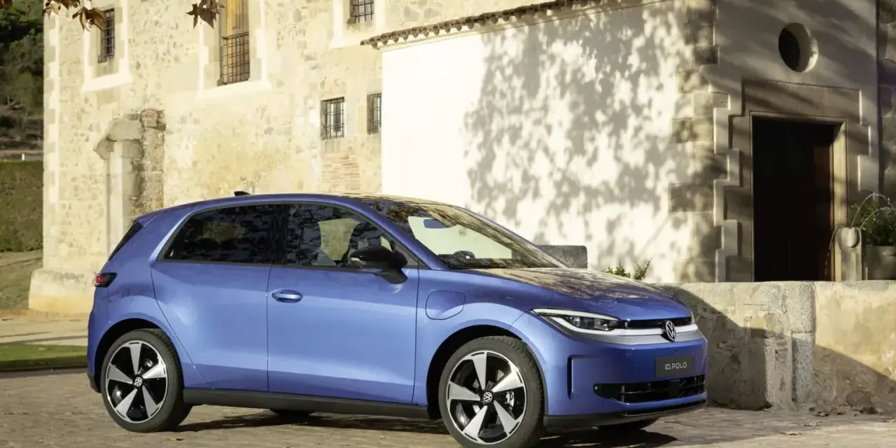 Niebieski samochód elektryczny VW ID. Polo stoi na brukowanej drodze przed kamiennym budynkiem.