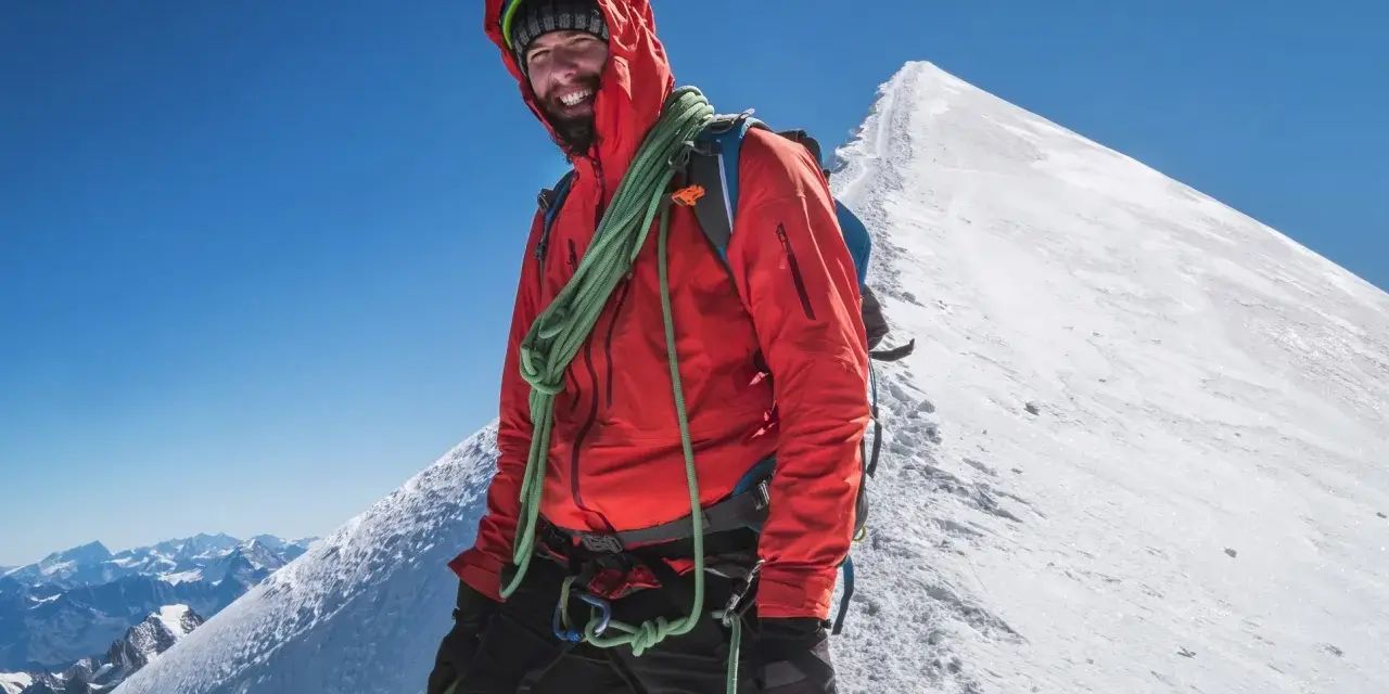 Uśmiechnięty alpinista na szczycie Mont Blanc, w czerwonej kurtce i z liną, gotowy na dalszą wspinaczkę.