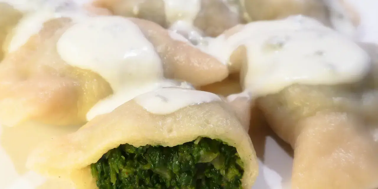 Pierogi ze szpinakiem polane sosem śmietanowym na białym talerzu.