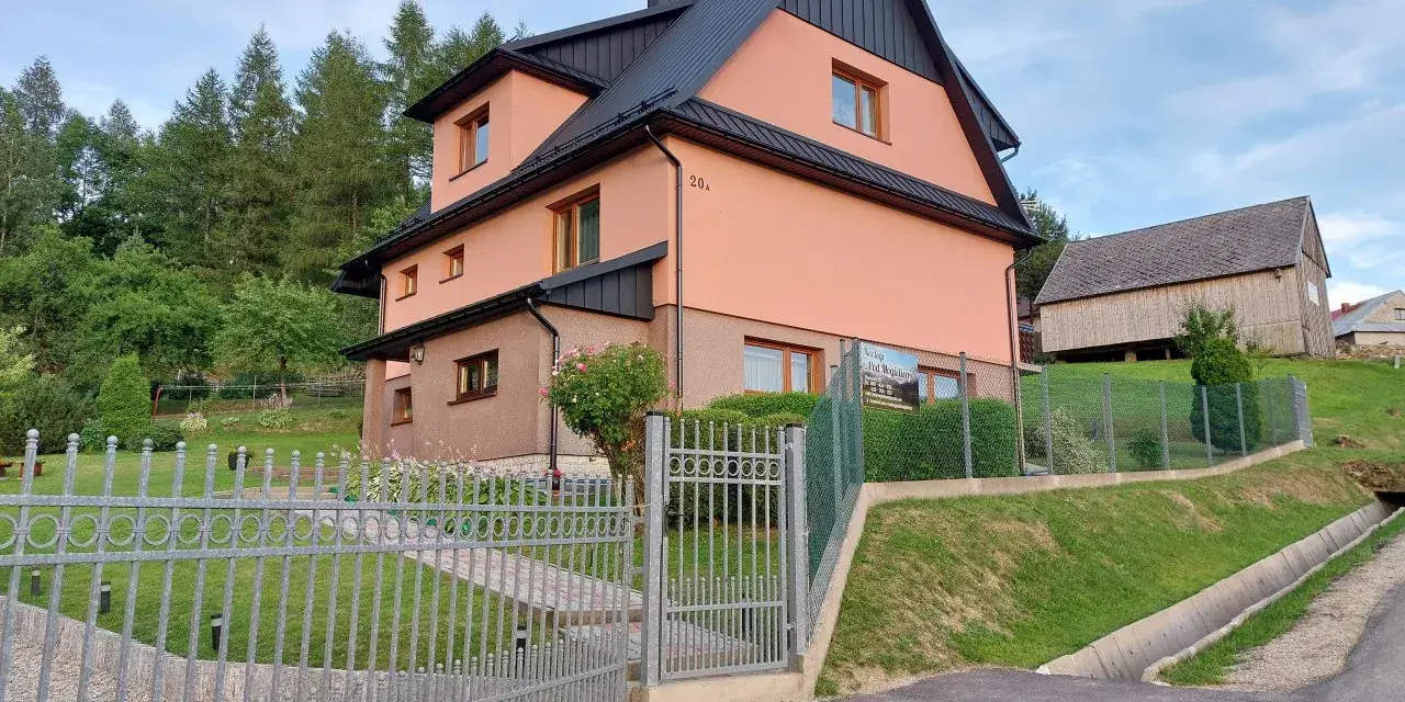 Urocze **mogielica schronisko** w otoczeniu zieleni. Jasnoróżowy budynek z czarnym dachem, obok drewniana stodoła.
