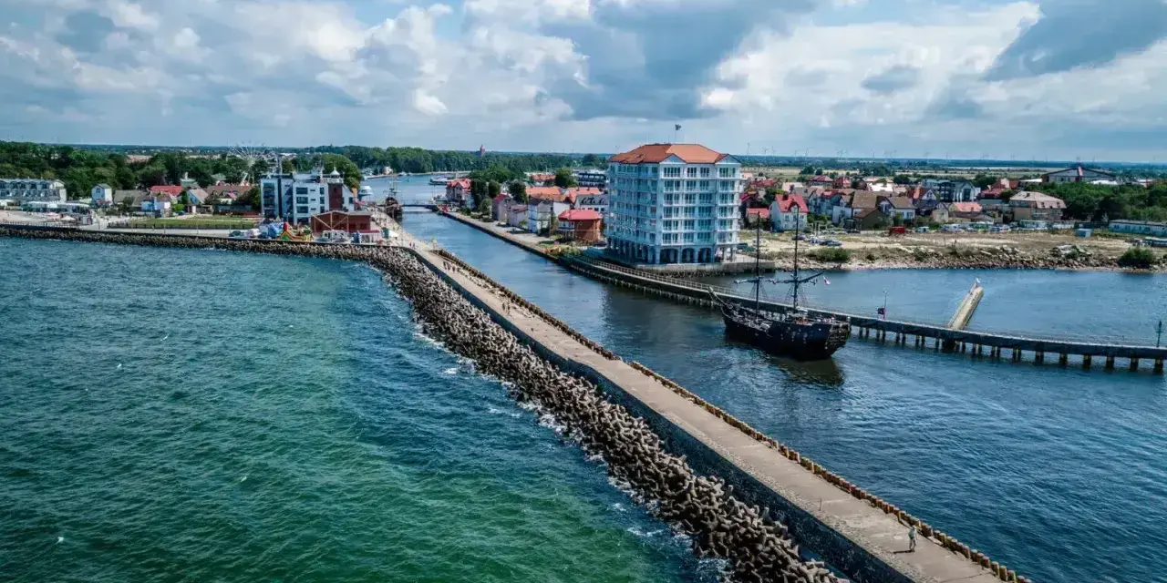 Widok na port w Darłówku z falochronem, statkiem pirackim i nowoczesnym budynkiem.