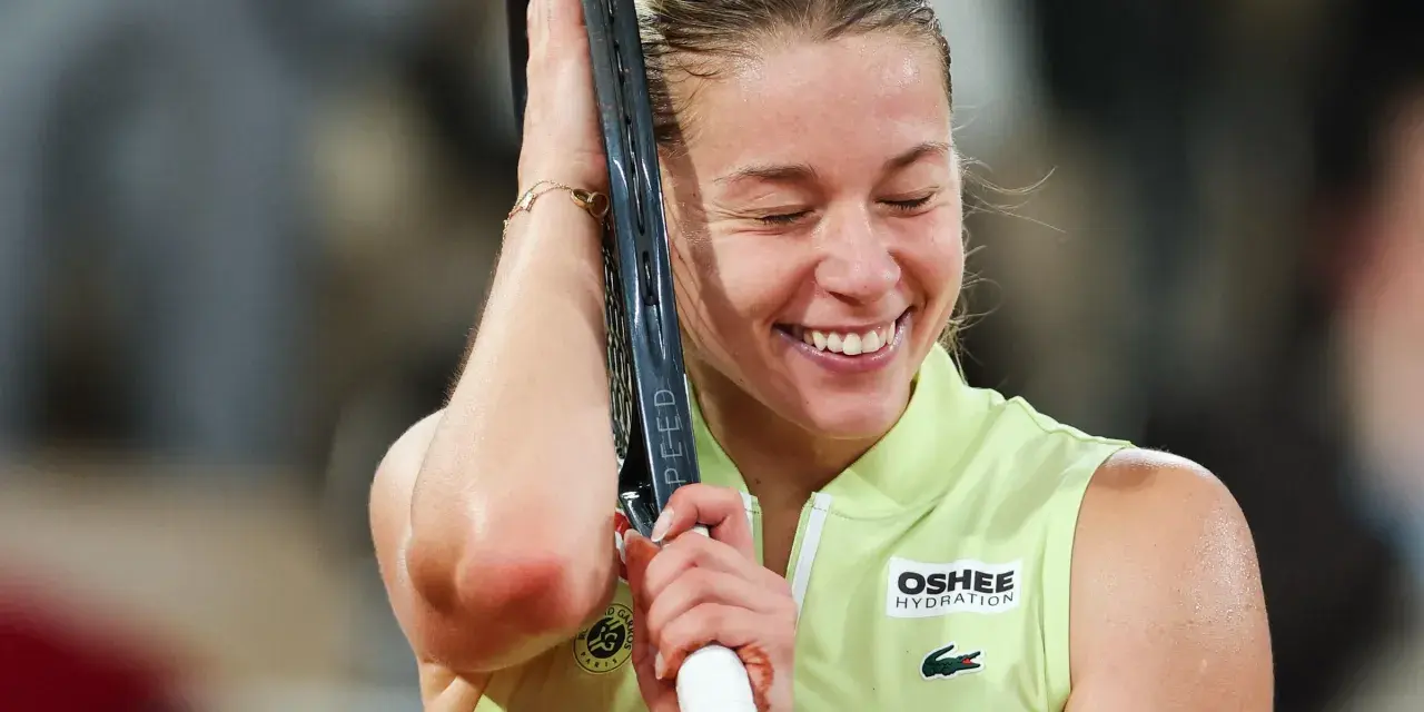 Szczęśliwa Iga Świątek, zwyciężczyni Roland Garros, z rakietą opartą o głowę, w geście triumfu.