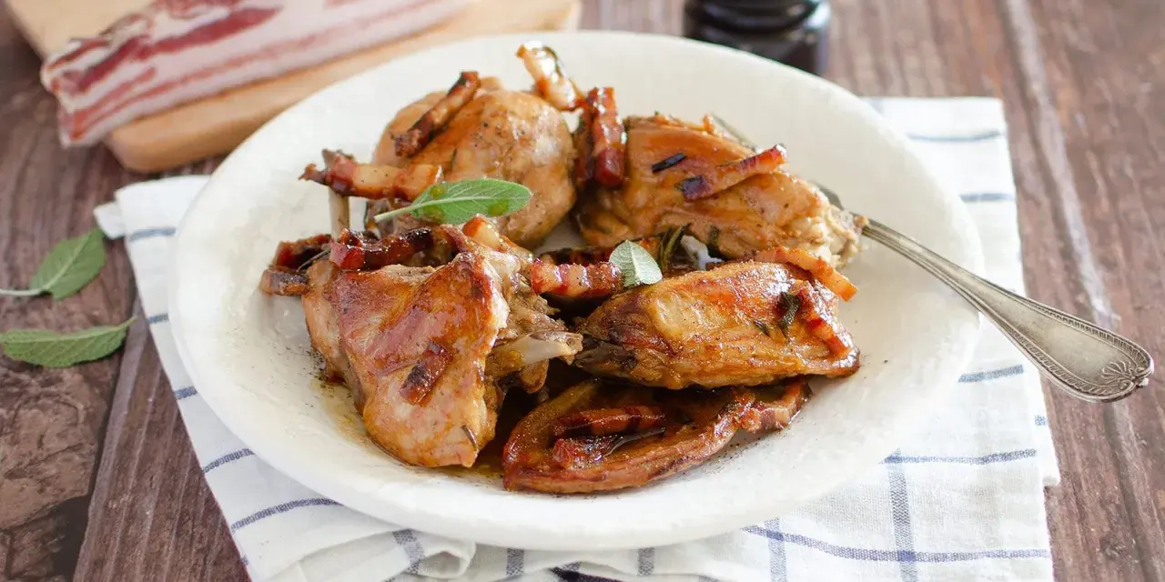Delizioso coniglio in padella, dorato e succulento, guarnito con pancetta croccante e foglie di salvia fresca.