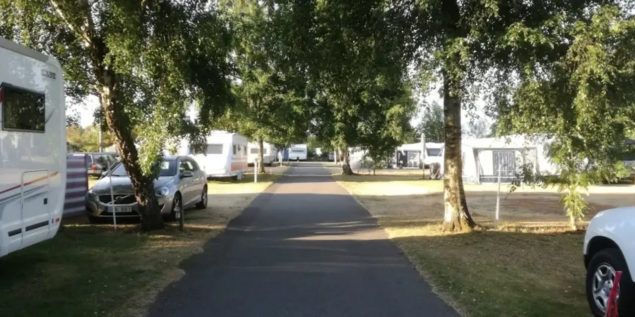 Väg leder genom rosendals camping, kantad av träd och husvagnar.