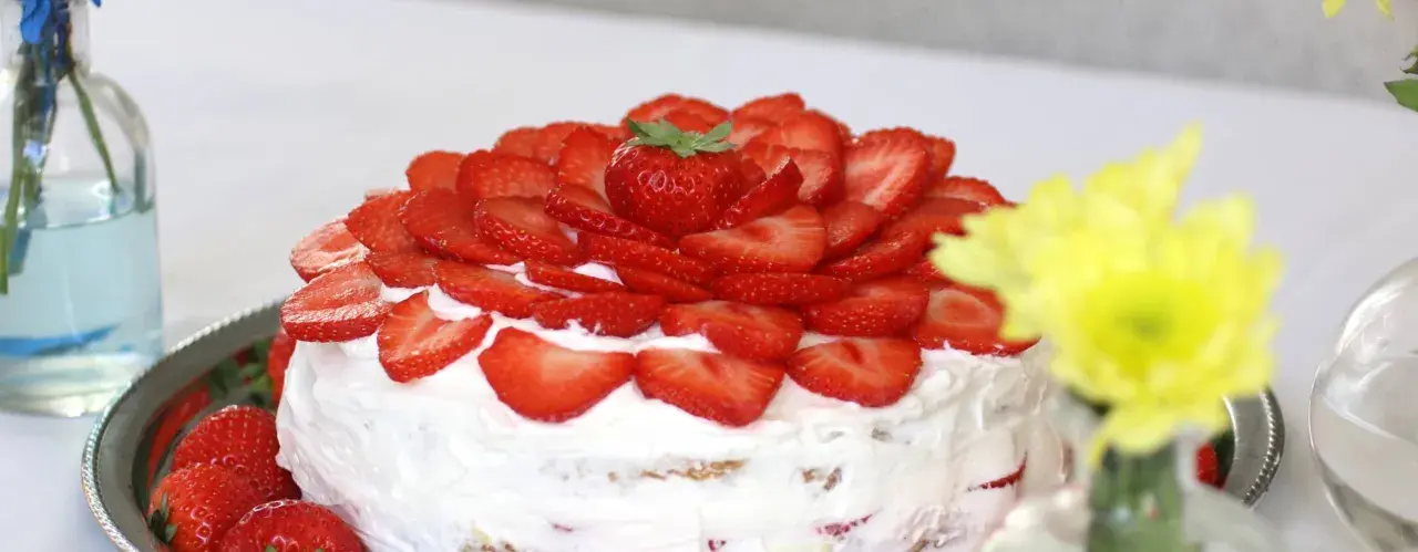En vacker vegansk jordgubbstårta täckt med färska jordgubbar och fluffig grädde. Perfekt för sommaren!