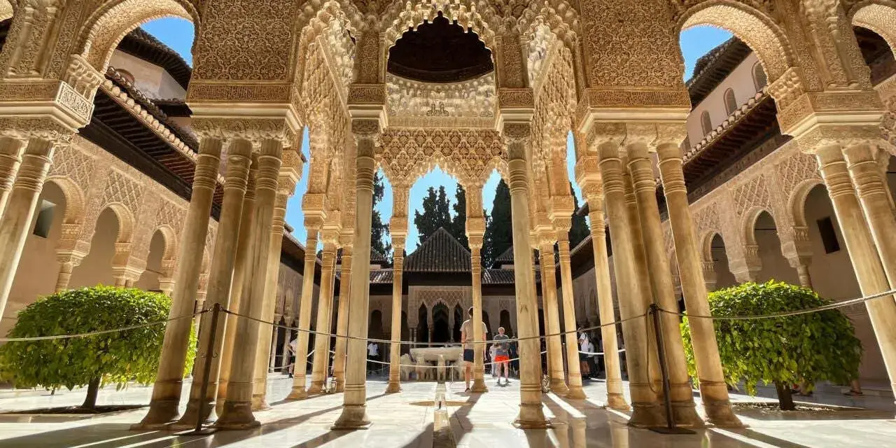 Intricate arches and columns of the Alhambra, a perfect postcard from Granada. Sunlight streams through, illuminating the detailed stonework.