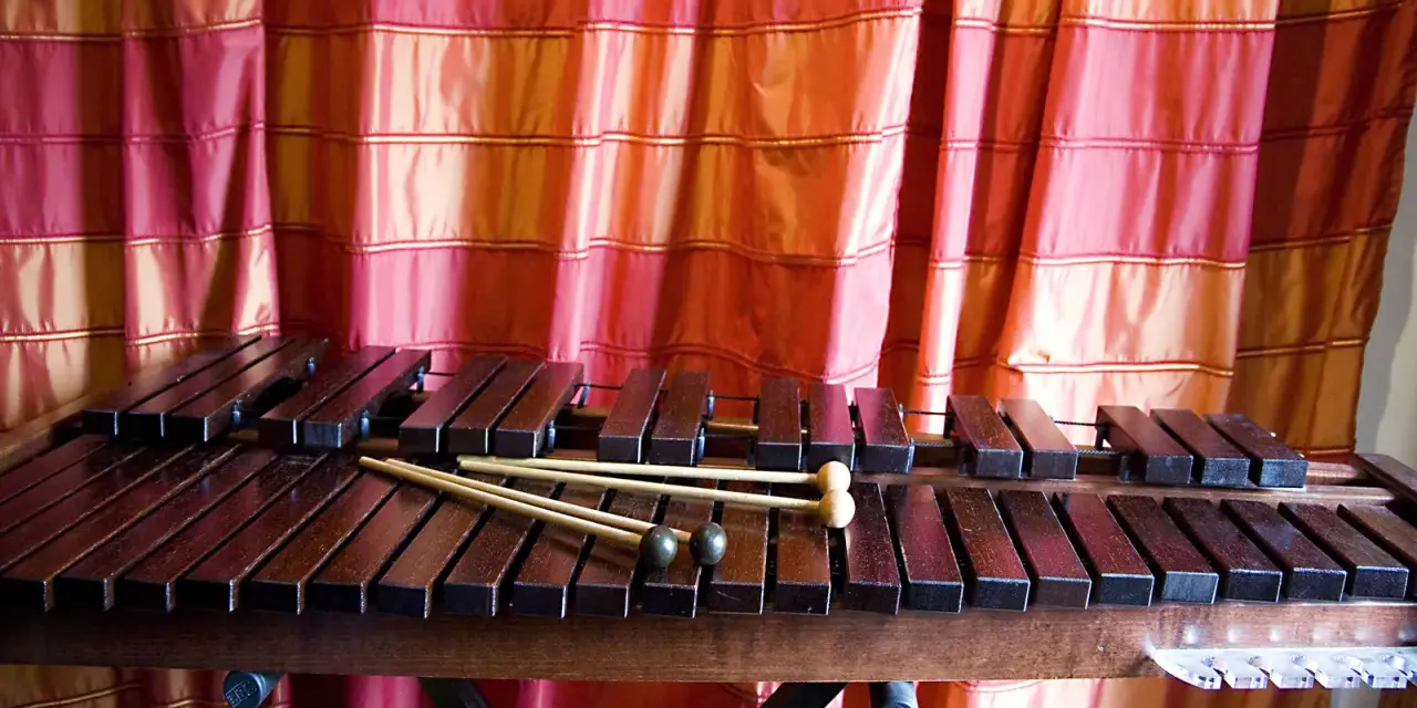 Ksylofon, instrument muzyczny na literę K, z pałeczkami, na tle czerwonej zasłony.