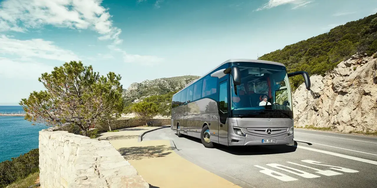 Srebrny Mercedes Tourismo jedzie malowniczą trasą nad morzem.