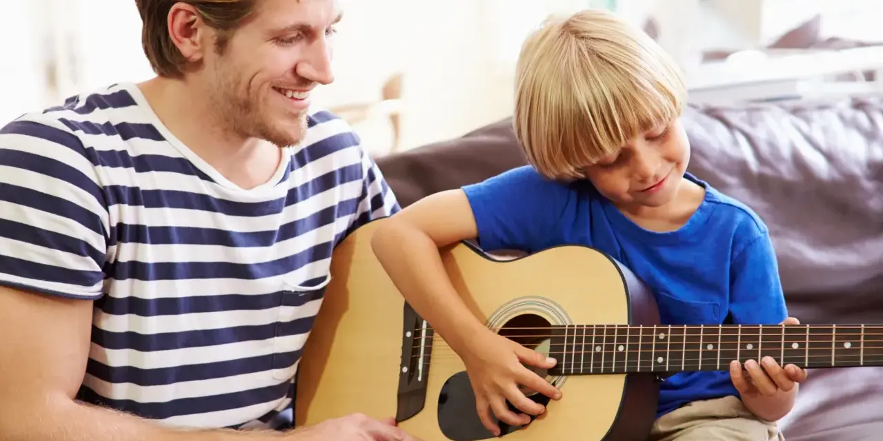 Ojciec uczy syna grać na gitarze. Radosna szkoła gry na gitarze w domowym zaciszu.