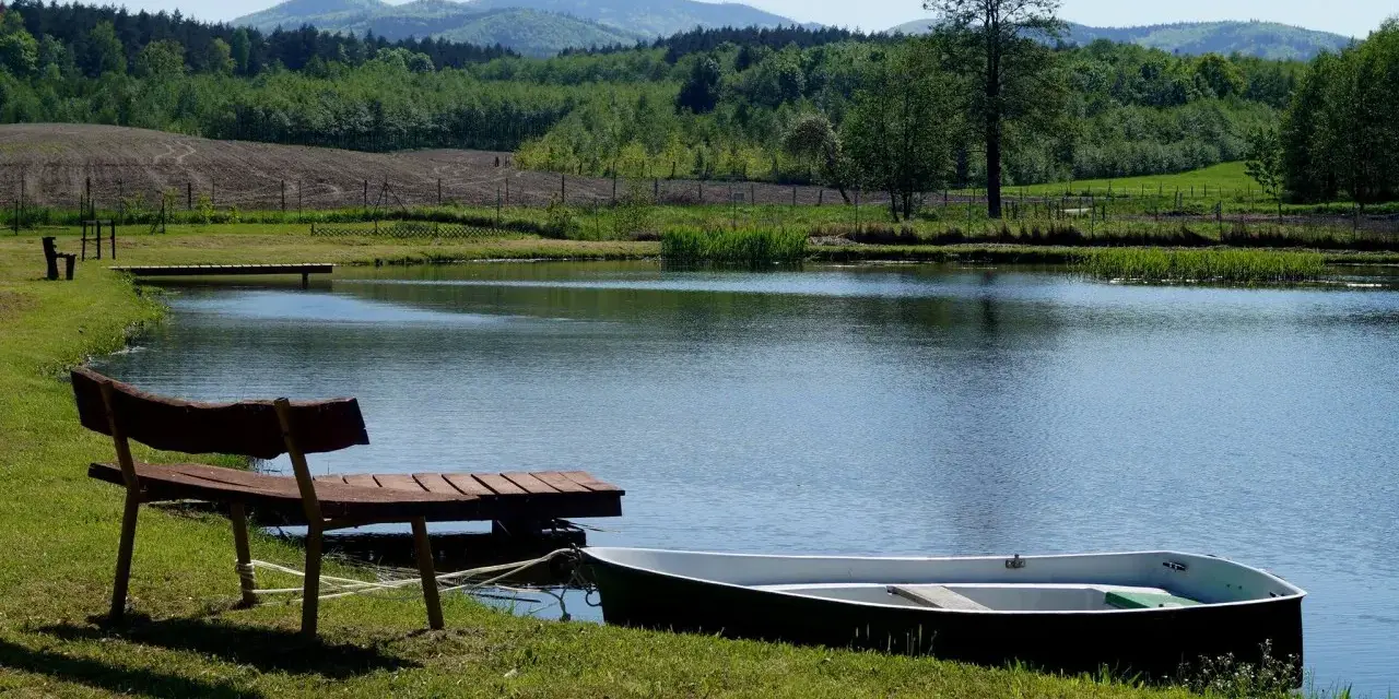 Idealne miejsce na camping nad stawami: łódka przy pomoście, ławka i spokojna tafla wody.