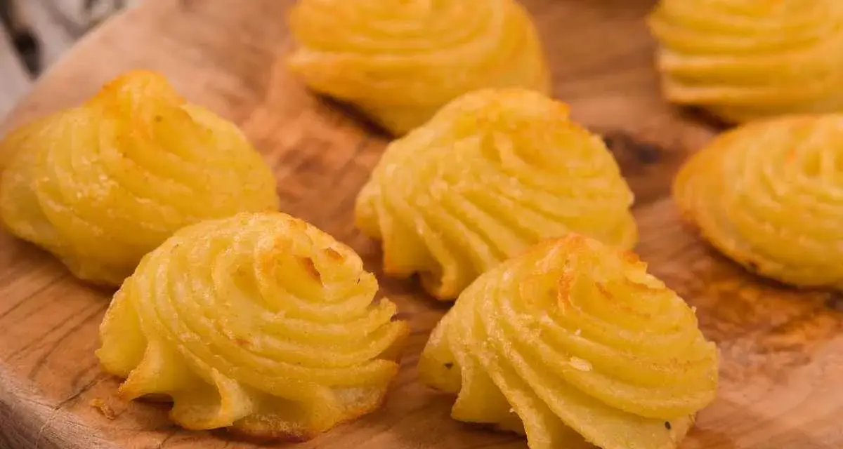 Patate duchessa dorate e invitanti, disposte su un tagliere di legno, pronte per essere gustate.