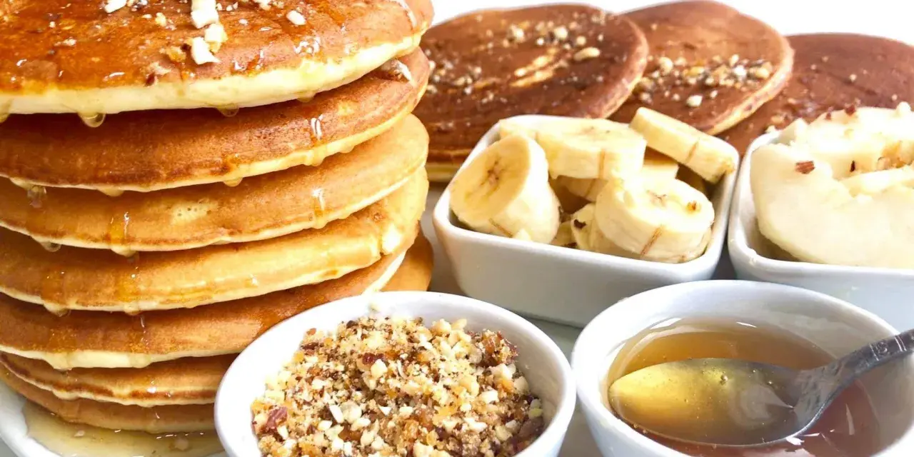 Pile de pancakes dorés arrosés de miel, accompagnés de rondelles de banane, de noix concassées et d'une cuillère de miel. Un délice pour le petit-déjeuner !