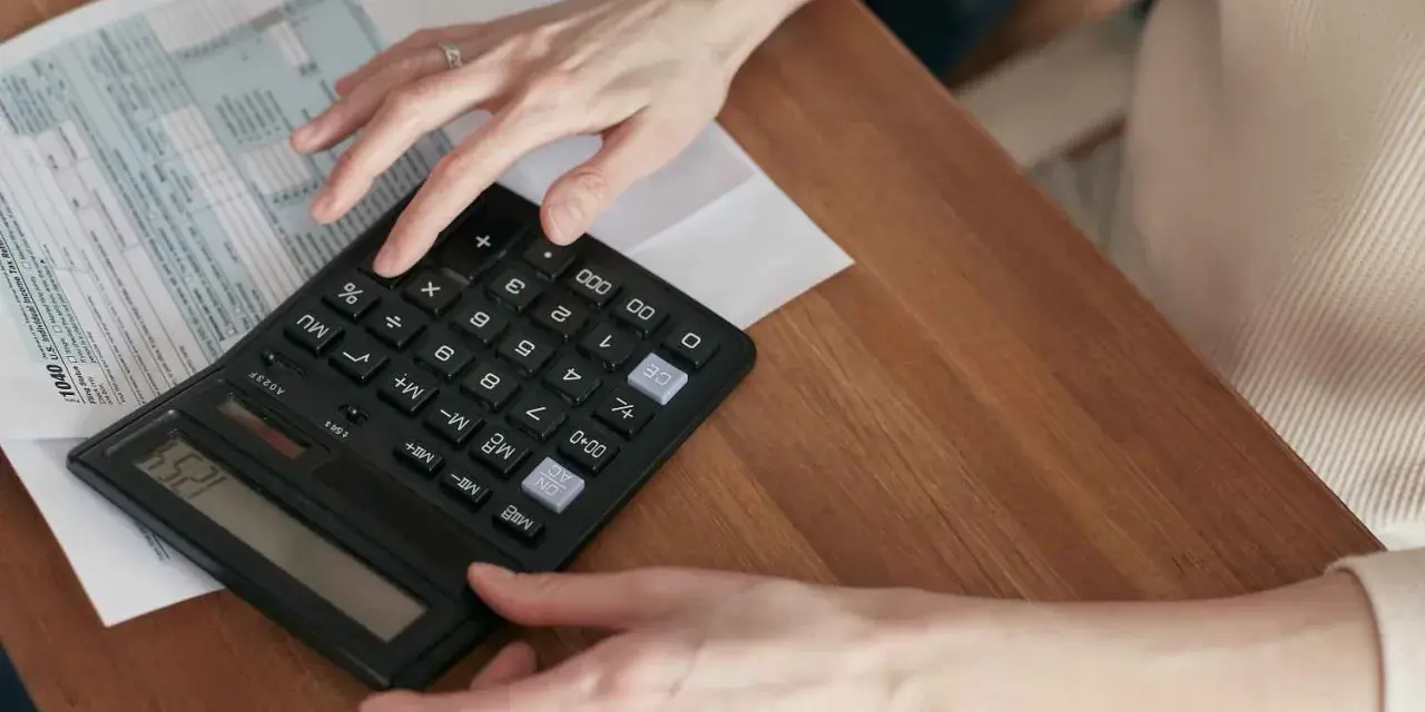 Manos calculando el total de suplidos en un formulario fiscal.