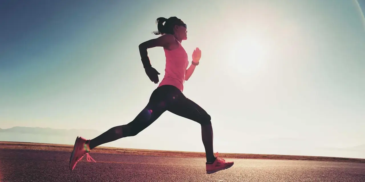 Donna corre su strada asfaltata al tramonto, con il sole che illumina la scena. Questo è un esempio di tempo run, un allenamento per migliorare la velocità.