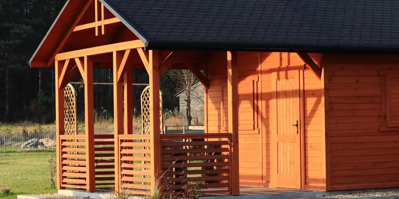 Drewniany dom szkieletowy z werandą i czarnym dachem, otoczony zieloną trawą.
