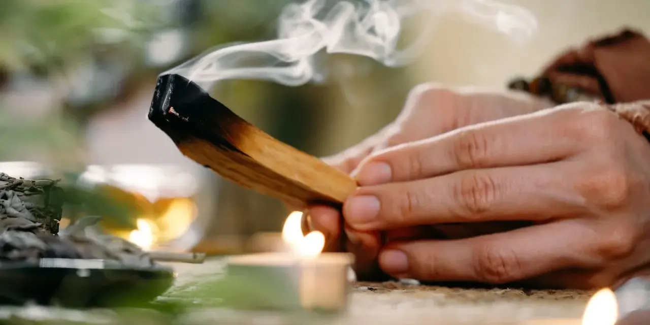 Dym z palo santo unosi się nad płonącą świecą. Zastanawiasz się, palo santo dlaczego nie używać?