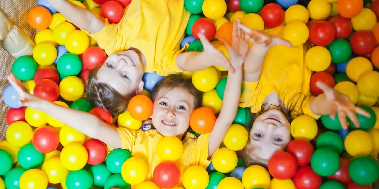 Drei Kinder in gelben T-Shirts spielen in einem Bällebad. Perfekte Ausflugsziele mit Kindern für Spaß und Lachen.