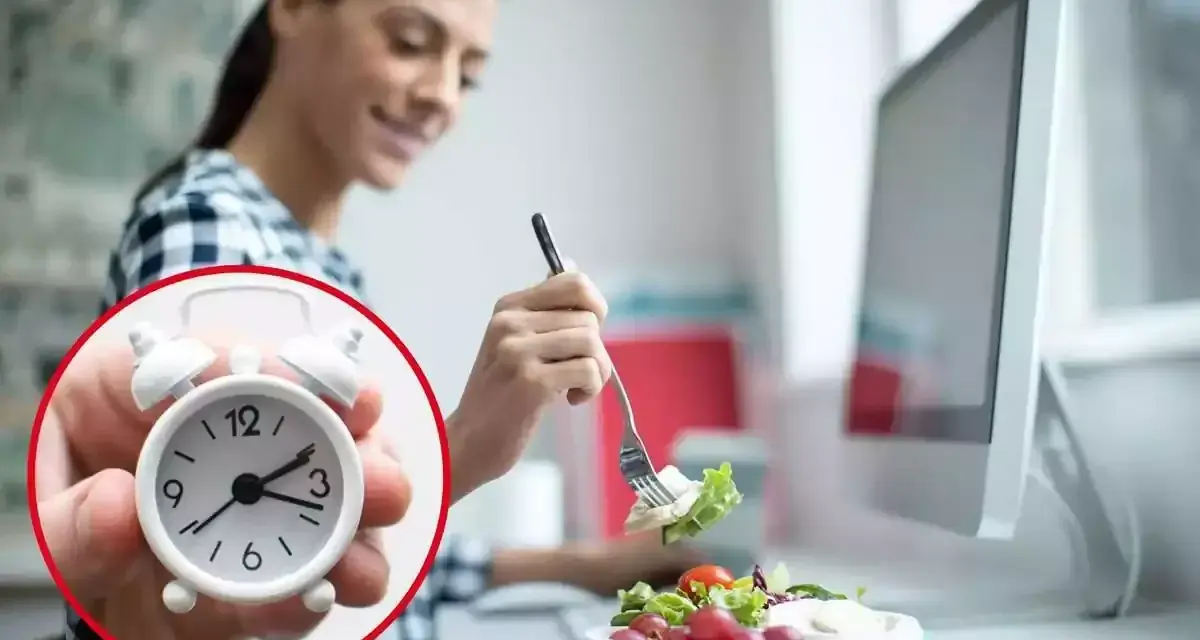 Mujer comiendo ensalada en su escritorio, con un reloj que marca el tiempo para comer en el trabajo.