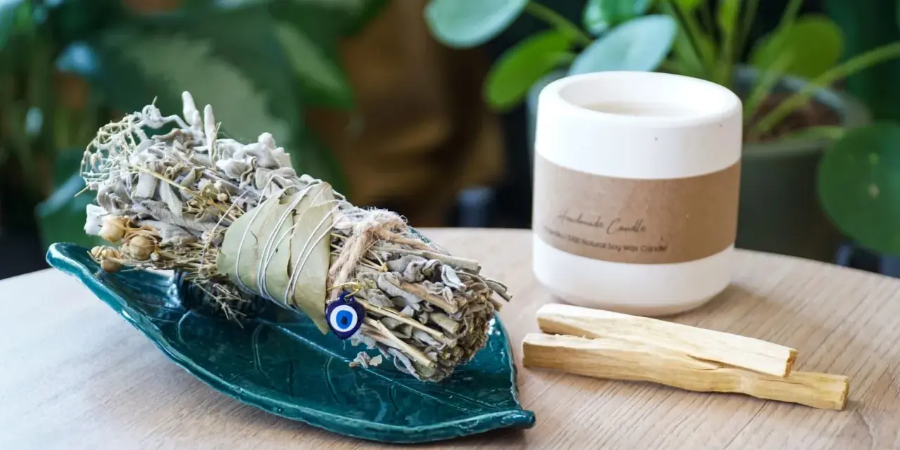 Ziołowe kadzidło na zielonej podstawce, obok świeca i patyczki palo santo. Idealne do rytuału, jak zrobić kadzidło.