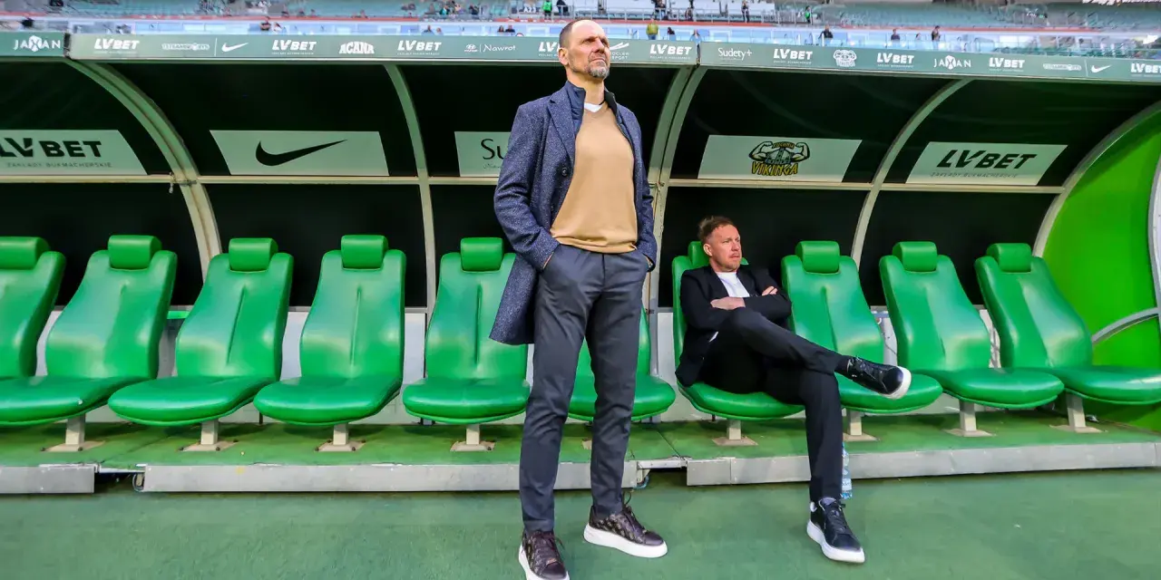 Trener Śląska Wrocław Ivan Djurdjevic stoi na tle zielonych siedzeń rezerwowych.