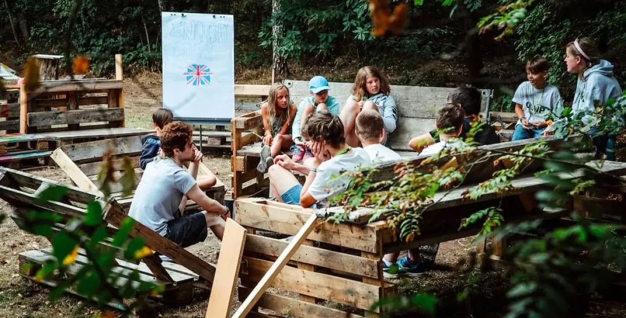 Kinder lernen im Freien beim englisch camp. Eine Tafel mit der britischen Flagge steht im Hintergrund.