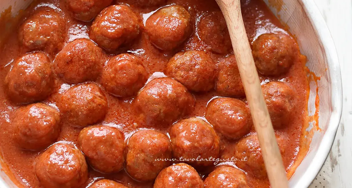 Polpette al sugo fumanti in una ciotola, pronte per essere gustate. Un cucchiaio di legno le accompagna.