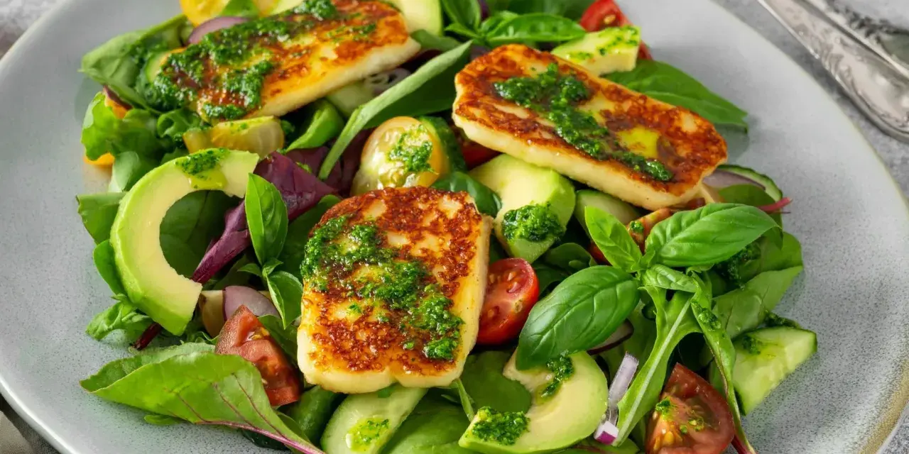Kolorowa sałatka z grillowanym halloumi, awokado, pomidorkami i ogórkiem, polana zielonym sosem.