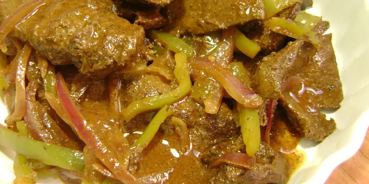Hígado guisado con cebolla y pimientos verdes en salsa marrón.